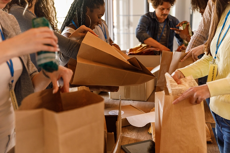 Group of dedicated volunteers thoughtfully arranging various food items, creating a diverse range of care packages for families facing hardship.